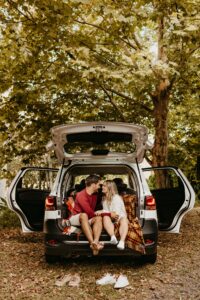 Marriage Enrichment Two youthful adults are sitting in the back of their hatchback car with the doors open shoes off they are having a loving conversation surrounded by fall leaves.